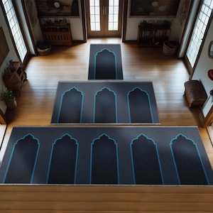 May include: A set of eight prayer rugs in a hallway. The rugs are arranged in a pyramid shape, with the largest rug at the bottom and the smallest rug at the top. The rugs are all black with blue trim and a decorative arch design.