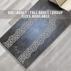 May include: A gray prayer rug with a white floral design and a white tassel fringe. The rug has a traditional prayer niche design. The text "Kid / Adult / Tall Adult / Group Sizes Available" is printed on the rug.