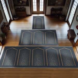 May include: A set of three dark grey prayer rugs with gold trim and a geometric pattern. The rugs are arranged in a staircase pattern, with the smallest rug at the top and the largest rug at the bottom.