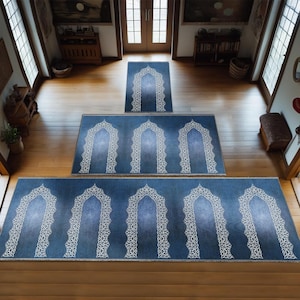 May include: A set of three blue prayer rugs with white geometric designs. The rugs are arranged in a staircase pattern on a wooden floor.