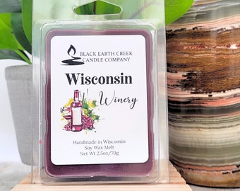 Könnte beinhalten: Ein violetter Sojawachs-Schmelz in einem durchsichtigen Plastikbehälter. Das Etikett lautet "Black Earth Creek Candle Company" und "Wisconsin Winery". Das Etikett zeigt auch eine handgezeichnete Illustration einer Weinflasche, eines Weinglases und Trauben. Der Schmelz ist handgefertigt in Wisconsin und wiegt 70 Gramm.