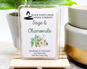 Könnte beinhalten: Eine transparente Kunststoffverpackung mit einem Sojawachs-Schmelzriegel. Das Etikett trägt die Aufschrift "Sage & Chamomile" mit einer floralen Illustration. Das Nettogewicht beträgt 70g. Auf einer kleinen Holzpalette platziert.