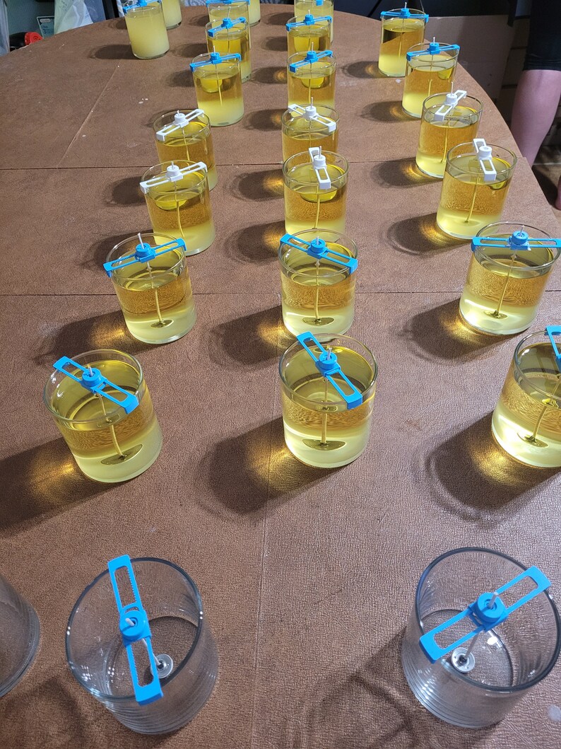 Pu&ograve; includere: Un piano con pi&ugrave; barattoli di vetro trasparente riempiti di un liquido giallo. Ogni barattolo ha un porta stoppino blu e bianco.