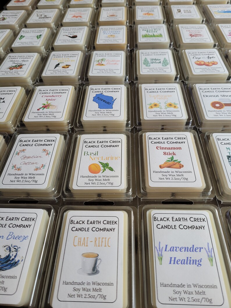 May include: An overhead shot of multiple soy wax melts in clear plastic containers. Each melt has a label with a unique scent name and graphic, such as "Cranberry Spice," "Basil Nectarine," and "Lavender Healing." The net weight is 2.5 oz / 70g.