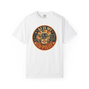 May include: A white short-sleeve t-shirt featuring a circular graphic on the chest. The design shows a cartoon robot holding a laptop, with the text AI IS MY CO-PILOT in a retro-style font, surrounded by a sunburst pattern and small stars.