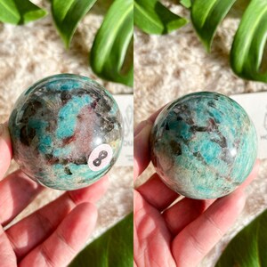 May include: A green, brown, and black sphere of Amazonite with a white sticker on it that says "8".