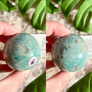 May include: A green and white amazonite sphere with a smooth, polished surface. The sphere is approximately 2 inches in diameter.