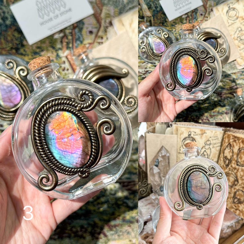May include: Clear glass bottle with a cork stopper and a decorative metal frame. The frame holds an oval-shaped, iridescent stone with colors of blue, purple, and orange. The bottle is labeled with the number "3".