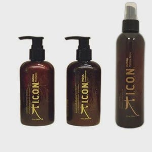 May include: Three brown bottles of hair care products with black pumps and spray nozzle. The bottles are labeled "ICON INDIA Shampoo", "ICON INDIA Conditioner", and "ICON INDIA Healing Spray". The bottles are on a light gray background.