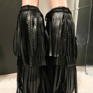 May include: Black ankle boots with layered fringe detailing. The boots have a textured, snake-like pattern and a delicate lace trim at the top. The fringe cascades down the front and sides, creating a bold, stylish look.