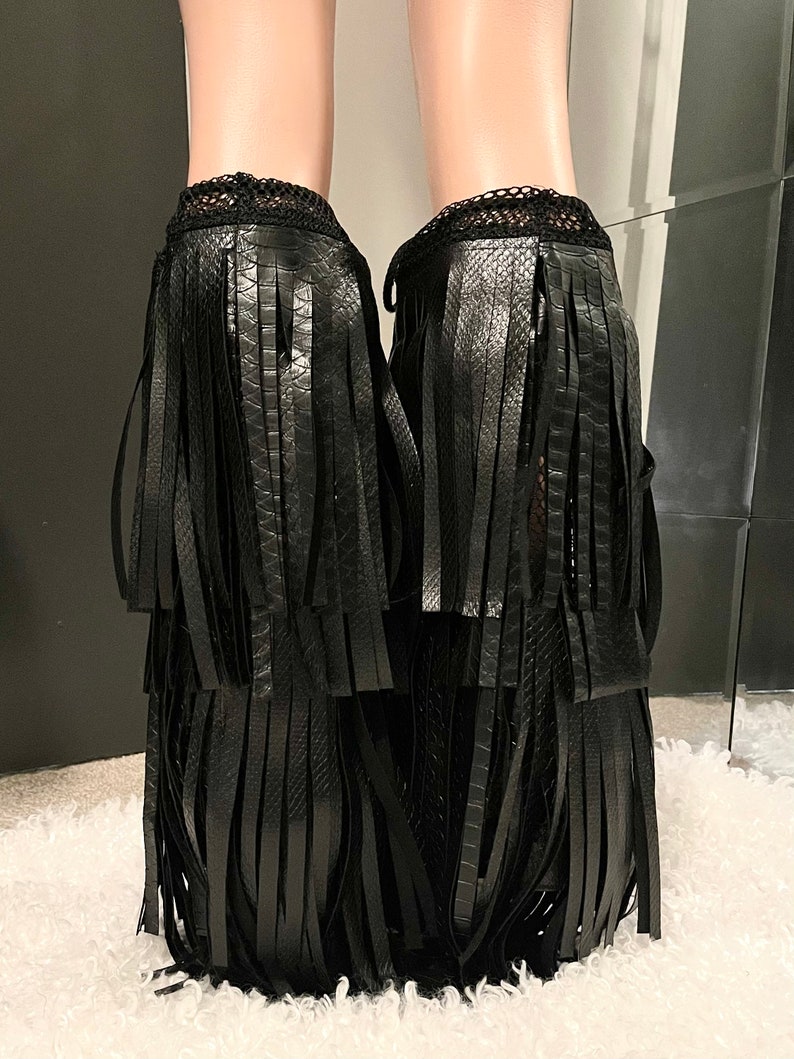 May include: Black ankle boots with layered fringe detailing. The boots have a textured, snake-like pattern and a delicate lace trim at the top. The fringe cascades down the front and sides, creating a bold, stylish look.