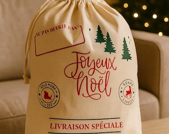 May include: A beige Christmas gift bag with a drawstring closure, decorated with red and green festive graphics. The bag has the words "Joyeux Noël" in red script, Christmas trees, and other text. It sits on a wooden table.