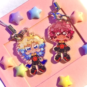 Peut inclure: Deux breloques en acrylique représentant des personnages de style anime avec des cheveux colorés et des uniformes sportifs assortis noirs, rouges et dorés. Chaque breloque comprend un fermoir mousqueton en métal argenté et un cordon blanc.