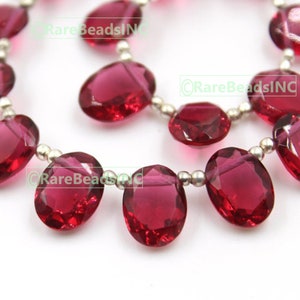 Może przedstawiać: Szereg owalnych, fasetowanych koralików z czerwonego kamienia szlachetnego nawleczonych na srebrny drut. Koraliki są półprzezroczyste i mają delikatny połysk.