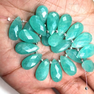 May include: A strand of faceted, pear-shaped amazonite beads in a vibrant teal-green color. The translucent gemstones are strung on a thin pink thread, interspersed with small, round, metallic silver spacer beads throughout the arrangement.