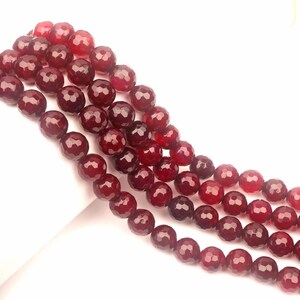 Puede incluir: Una hebra de cuentas de piedras preciosas facetadas de color rojo intenso. Las cuentas son redondas y tienen un acabado liso y pulido.