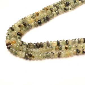 May include: A strand of green and brown gemstone beads. The beads are faceted and have a slightly irregular shape. The beads are strung on a clear thread.