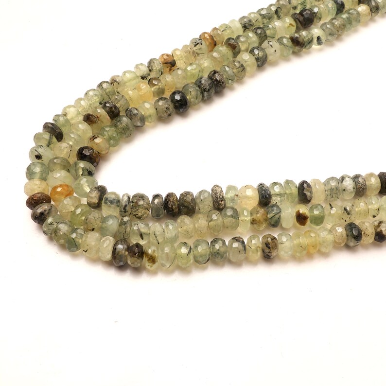 May include: A strand of green and brown gemstone beads. The beads are faceted and have a slightly irregular shape. The beads are strung on a clear thread.
