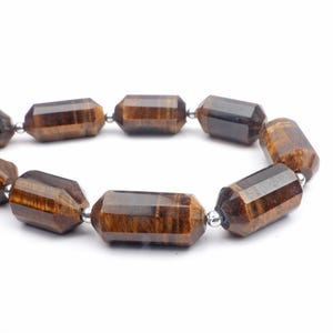 May include: A close-up of a bracelet made of faceted, brown tiger's eye beads. The beads are strung together with small, silver-colored metal beads. The bracelet is set against a white background.