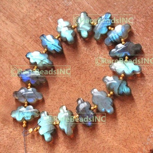 Peut inclure: Un collier de perles de labradorite en forme de nuage. Les perles sont un mélange de bleu, de gris et de sarcelle, avec des entretoises dorées. Les perles sont enfilées sur un fil fin et foncé, et sont exposées sur une surface en bois.