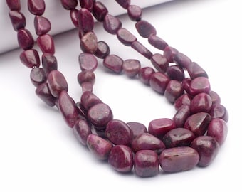 May include: Strands of polished, deep red ruby gemstone beads. The beads have a smooth, rounded shape and vary in size. The gemstones are strung together, creating a necklace or bracelet. The background is white.