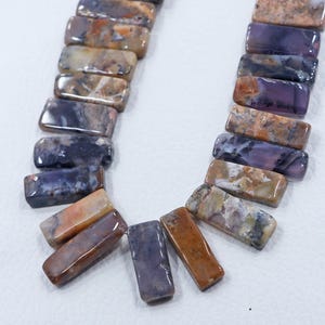 May include: A strand of purple, brown, and white agate gemstone beads. The beads are rectangular and have a polished finish.