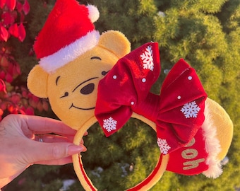 May include: Red and white Christmas Minnie Mouse ears with a plush Winnie the Pooh head wearing a Santa hat. The bow has snowflakes and the ear has the word "Hoof" on it.
