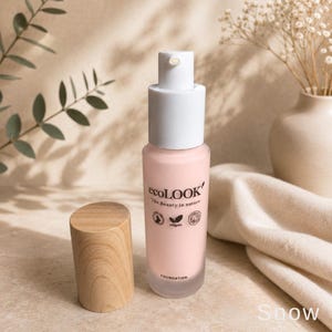 May include: A cylindrical glass bottle of light pink foundation with a white pump dispenser and a separate light wood cap. The label reads ecoLOOK The Beauty in nature, with small icons for vegan and cruelty-free certifications and the word FOUNDATION.