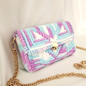 May include: A rectangular, handmade handbag with a gold chain strap. The bag is made of soft, textured yarn in shades of light blue, purple, and white. It features a gold clasp closure and a gold chain strap.
