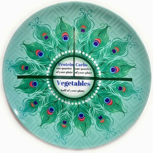 May include: A teal blue ceramic plate with a peacock feather design. The plate is divided into sections with the text "Protein one quarter of your plate", "Carbs one quarter of your plate", and "Vegetables half of your plate".