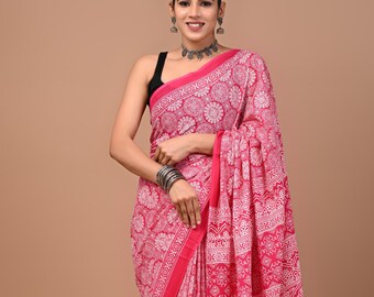 May include: A vibrant pink saree with a white floral pattern and a red border. The saree is draped over a person. A small wooden stool with a clay pot is in the background.