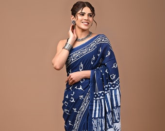 May include: A blue cotton saree with a white floral and geometric print. The saree is draped on a woman standing in front of a brown background.