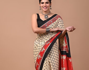 May include: A cream-colored saree with a black and red border. The saree has a geometric pattern and floral designs. The saree is draped on a woman standing in front of a beige background.