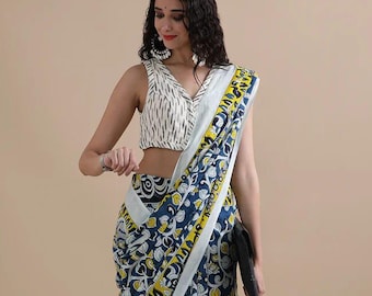 May include: A woman wearing a traditional Indian saree with a white and black patterned blouse. The saree features a navy blue background with yellow and white floral patterns. The border is white with yellow accents. She is holding a black clutch.