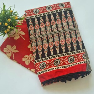 May include: A red and black cotton fabric with a floral pattern. The fabric has a fringe border and is folded in half.