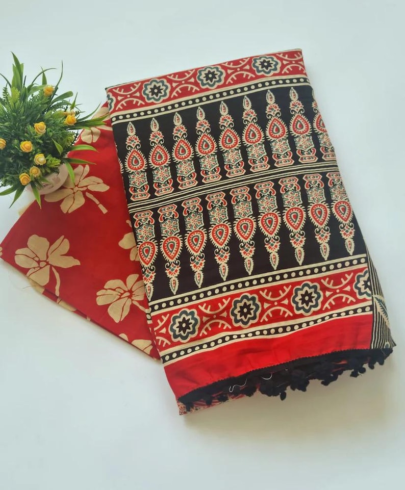 May include: A red and black cotton fabric with a floral pattern. The fabric has a fringe border and is folded in half.