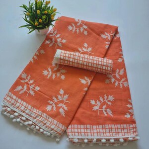 May include: Orange cotton saree with white leaf print and white checkered border. The saree has a white pom-pom trim.