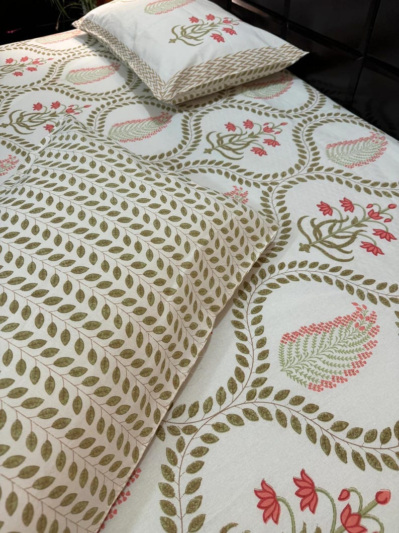 May include: White bed linen set featuring a floral design in red, green, and beige. The set includes a pillow and a fitted sheet. The pillow has a beige border. The fitted sheet has a repeating floral pattern.