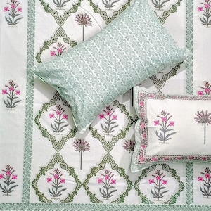 May include: White bed linen set featuring a floral design in pink and grey. The set includes two pillowcases, one in a solid pale green and the other with a floral border. The bedspread has a repeating floral pattern.
