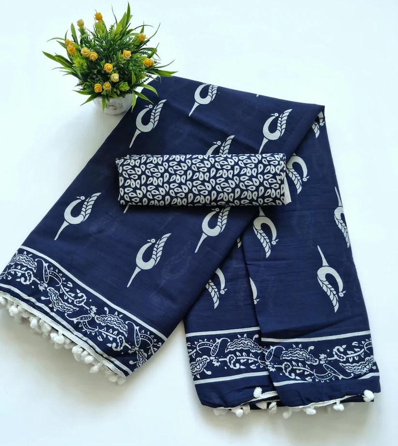 May include: A navy blue cotton saree with a white floral print and white pom-poms along the border. The saree comes with a matching blouse piece.