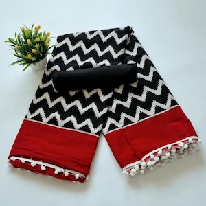 May include: Black and white zig zag patterned fabric with a red border and white pom pom trim. The fabric is folded in half and a black fabric piece is placed on top.