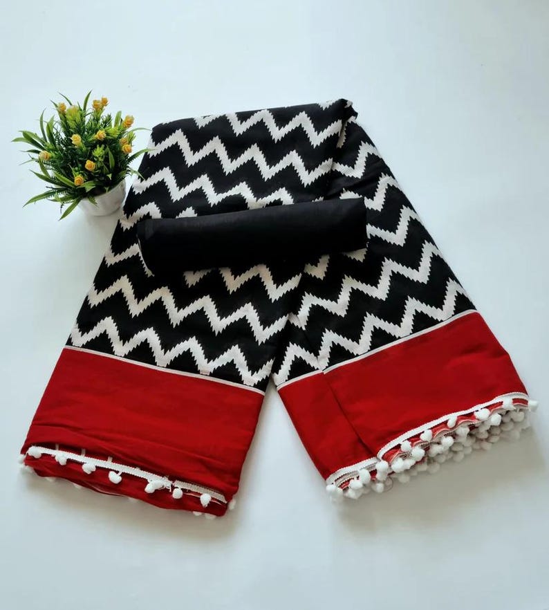May include: Black and white zig zag patterned fabric with a red border and white pom pom trim. The fabric is folded in half and a black fabric piece is placed on top.