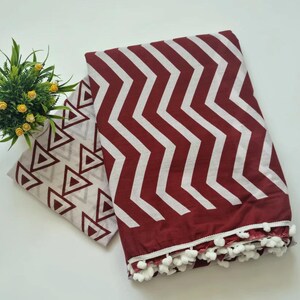 May include: A maroon and white cotton scarf with a chevron pattern and white pom-poms around the edge. The scarf is folded in half and has a white and gray triangle pattern on the inside.