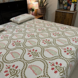 May include: White bed linen set featuring a repeating pattern of red flowers and green leaves within a circular design, outlined with a brown border. The bed is against a black headboard. The room has a floral wallpaper.