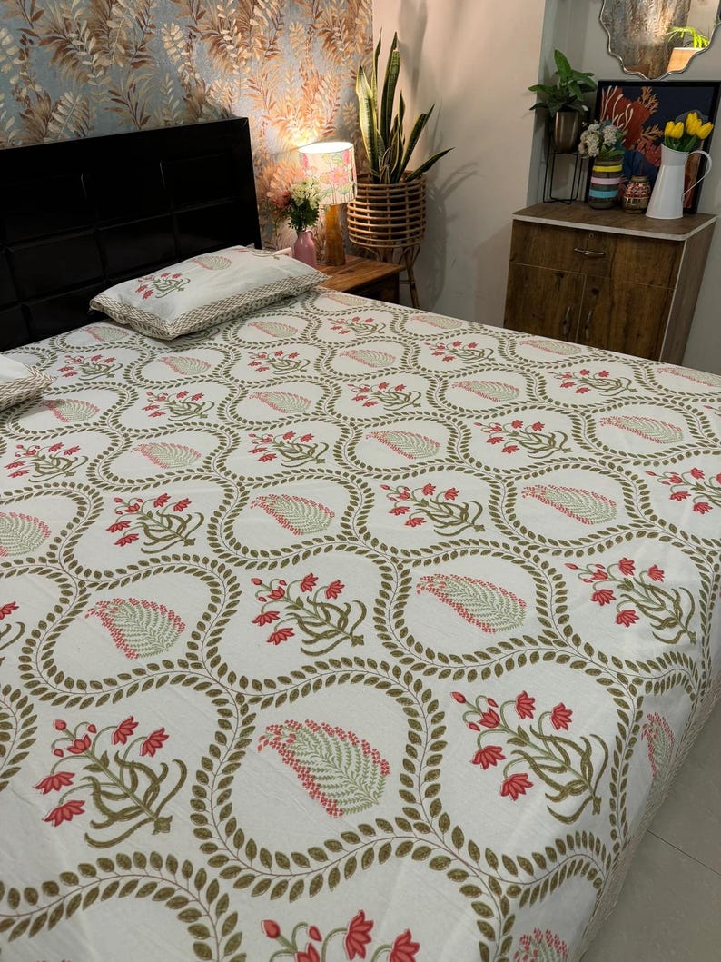 May include: White bed linen set featuring a repeating pattern of red flowers and green leaves within a circular design, outlined with a brown border. The bed is against a black headboard. The room has a floral wallpaper.