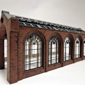 Op de afbeelding: Een rood bakstenen modelgebouw met een grijs dak en gebogen ramen. Het gebouw heeft een gedetailleerde bakstenen gevel en een eenvoudig, modern ontwerp.