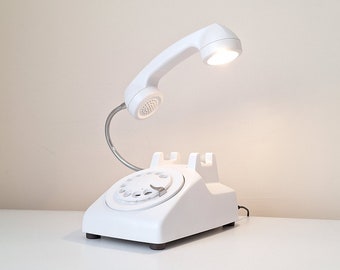 May include: White rotary phone shaped desk lamp with a flexible arm and a white light bulb.
