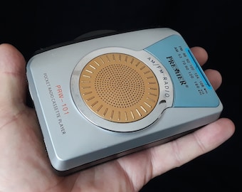 May include: A silver and blue pocket radio cassette player with the text "PREMIER AM/FM RADIO" and "PRW-101 POCKET RADIO CASSETTE PLAYER". The radio has a dial with frequency markings for AM and FM bands.