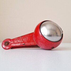 May include: A red metal jingle bell with a silver bell inside. The bell is attached to a red metal handle.