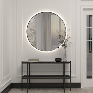 Round color mirror in metal black frame backlit by LED, visible division into two types of mirrors